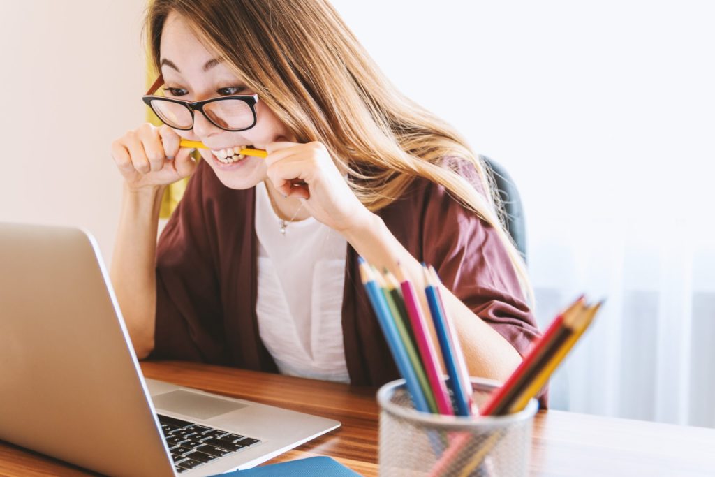 woman on eyeglasses studying on her laptop while biting pencil